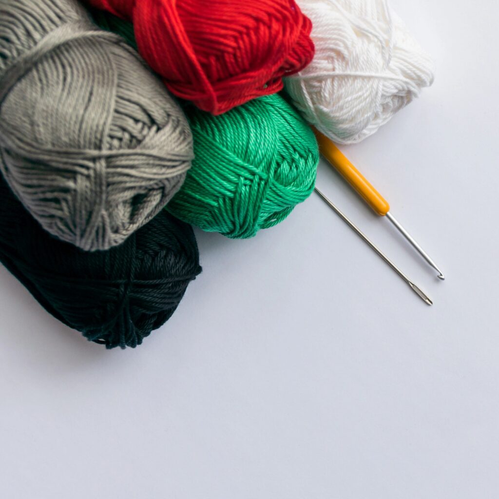 Colorful Balls of yarn with crochet hook and needle, flat lay on a white background